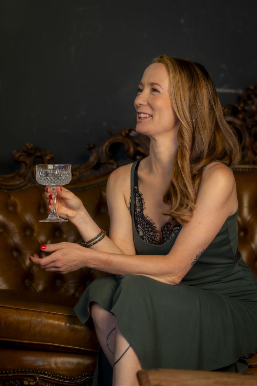 Frau auf Ledersofa, lächelnd mit Glas in eleganter Umgebung.