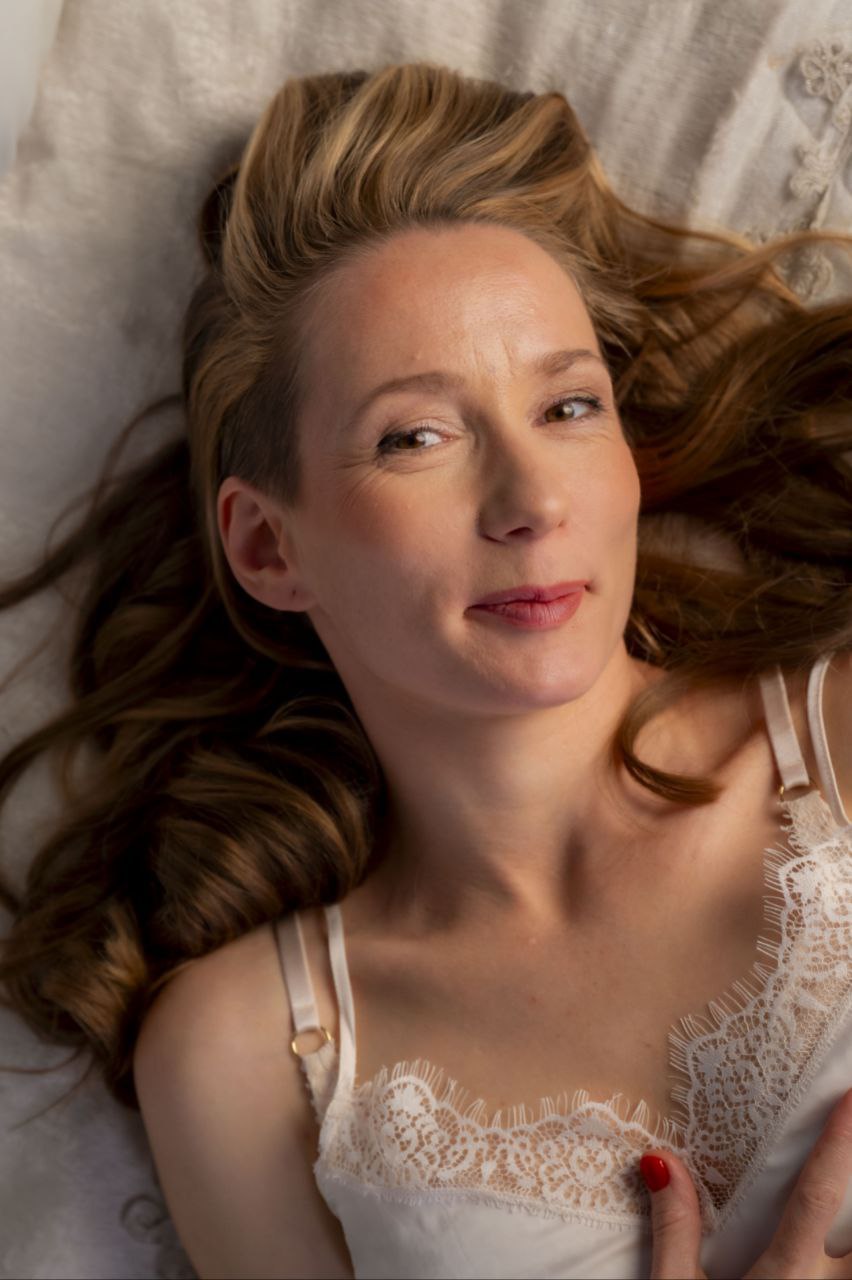 Frau liegt auf Bettwäsche, sanfte Intimität und Wärme.